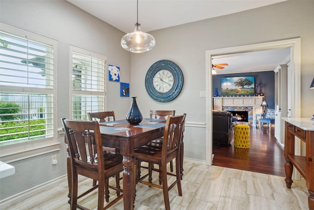 dining area featuring baseboards, a ceiling fan, a warm lit fireplace, and a wealth of natural light