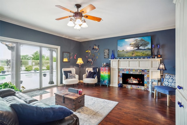 living room with a tiled fireplace, ceiling fan, ornamental molding, and wood finished floors