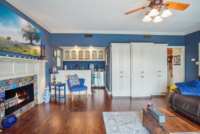 living area with ceiling fan, dark wood-style flooring, visible vents, crown molding, and a fireplace
