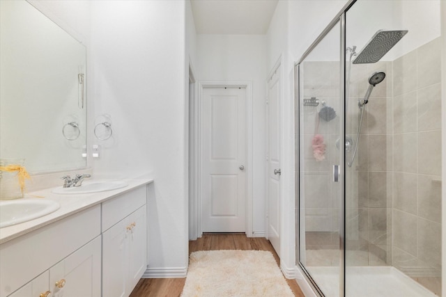 bathroom featuring a sink, double vanity, a shower stall, and wood finished floors