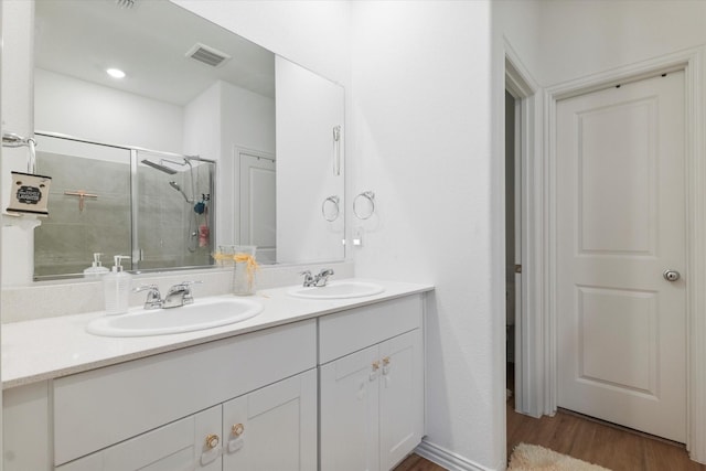 bathroom with double vanity, visible vents, a stall shower, wood finished floors, and a sink
