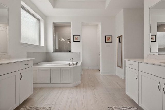 full bath with baseboards, a garden tub, a stall shower, and two vanities