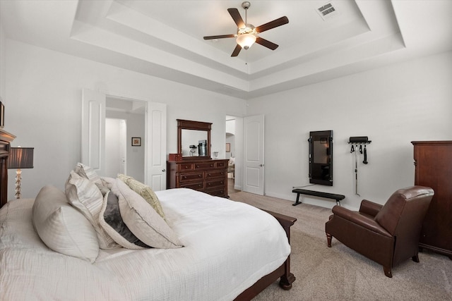 bedroom with a tray ceiling, visible vents, light carpet, and ceiling fan