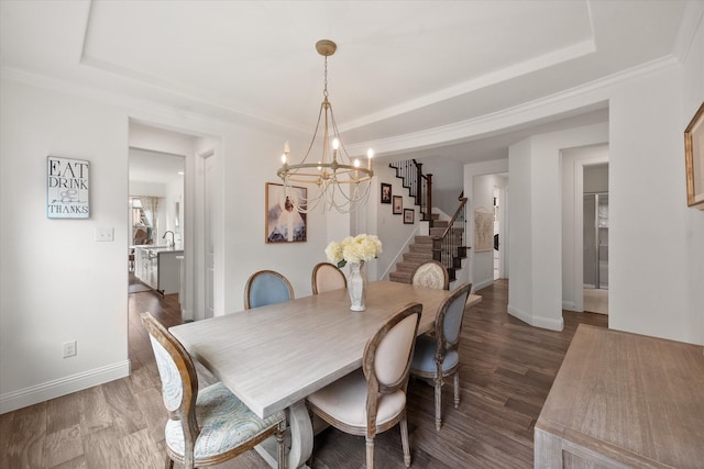 dining space with a tray ceiling, wood finished floors, a chandelier, and stairway