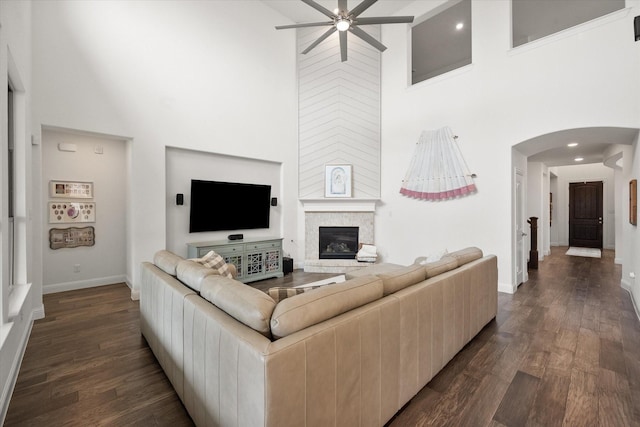 living room featuring ceiling fan, a high ceiling, arched walkways, dark wood finished floors, and baseboards