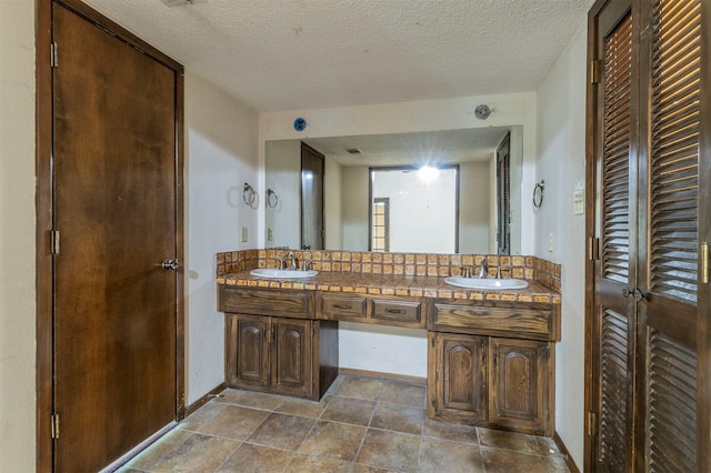 full bathroom featuring double vanity, a textured ceiling, baseboards, and a sink