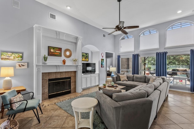living area featuring ceiling fan, visible vents, light tile patterned flooring, a fireplace, and a high ceiling