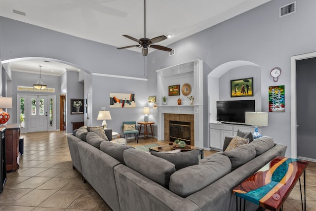 living area featuring a tiled fireplace, visible vents, ceiling fan, arched walkways, and light tile patterned flooring