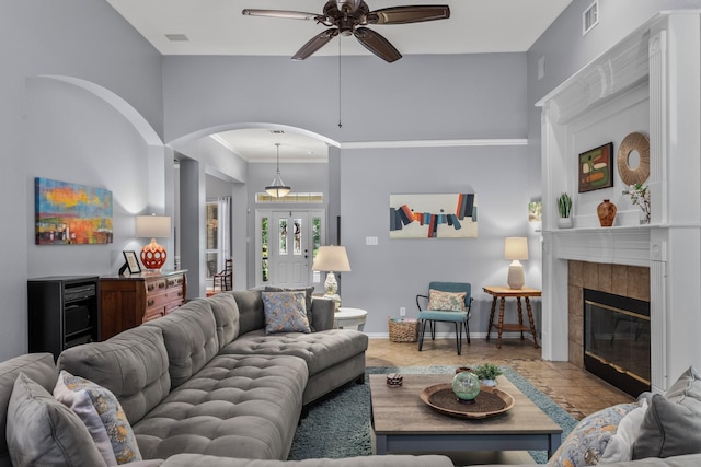 living area with ornamental molding, a fireplace, arched walkways, a ceiling fan, and baseboards