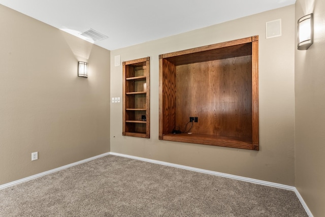 carpeted spare room with built in shelves and baseboards