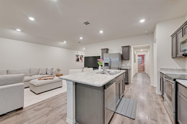 kitchen with a sink, stainless steel appliances, light wood-type flooring, and an island with sink