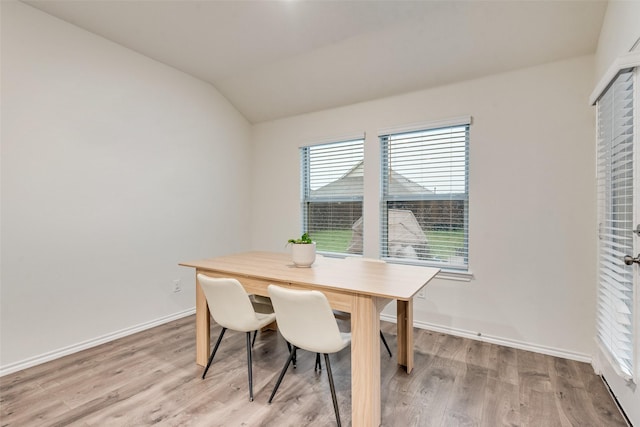dining area featuring baseboards, light wood finished floors, and vaulted ceiling