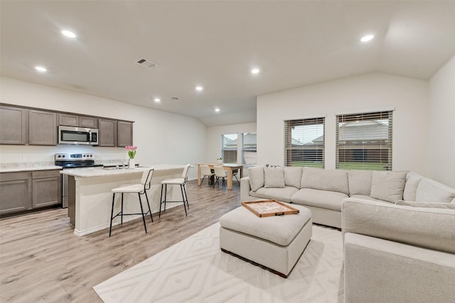 living area featuring visible vents, recessed lighting, light wood-style flooring, and vaulted ceiling