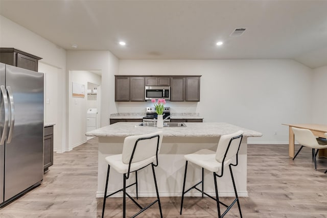 kitchen featuring a kitchen island with sink, visible vents, appliances with stainless steel finishes, dark brown cabinets, and a sink