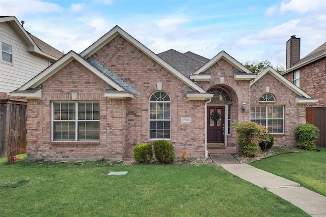 view of front of home featuring brick siding, roof with shingles, fence, and a front yard