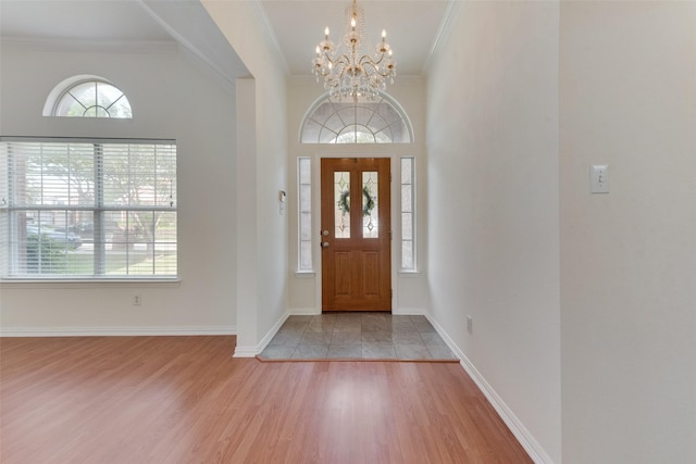 entrance foyer with crown molding, a chandelier, a healthy amount of sunlight, and wood finished floors