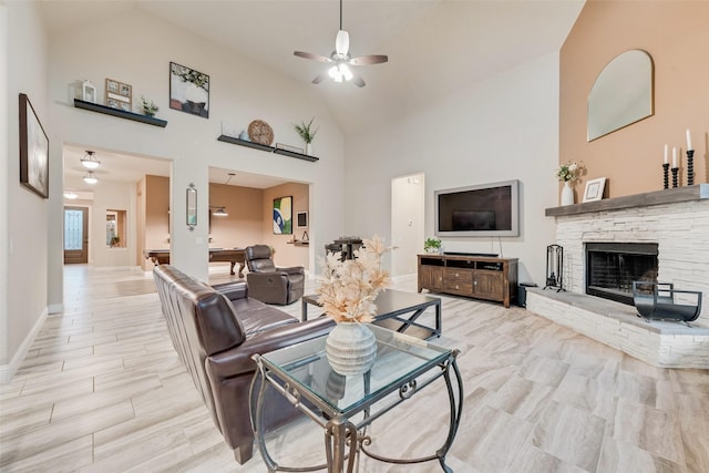 living room featuring high vaulted ceiling, a stone fireplace, ceiling fan, and baseboards