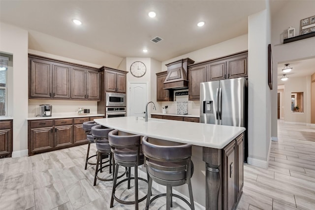 kitchen featuring custom exhaust hood, stainless steel appliances, light countertops, a sink, and a breakfast bar