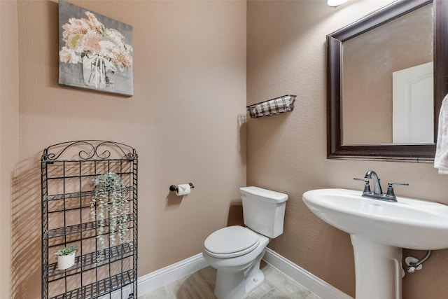 half bath featuring toilet, baseboards, and a sink