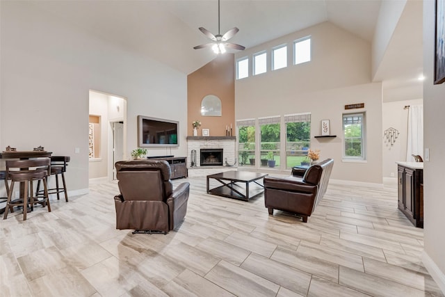 living room with a ceiling fan, a stone fireplace, high vaulted ceiling, plenty of natural light, and baseboards