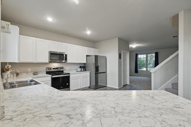 kitchen with baseboards, recessed lighting, white cabinets, a sink, and stainless steel appliances