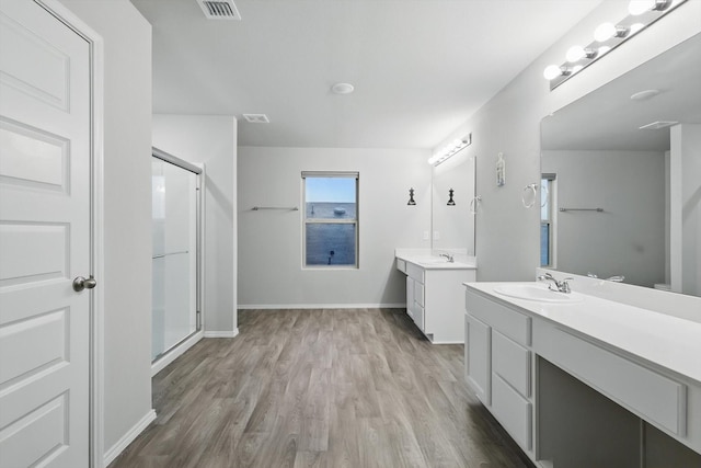 bathroom with visible vents, a shower stall, wood finished floors, two vanities, and a sink