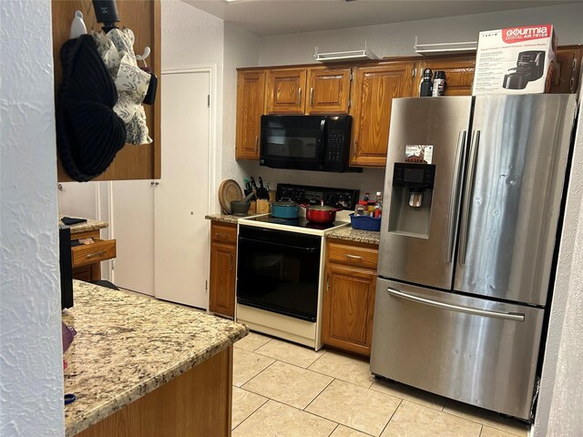 kitchen featuring light tile patterned floors, brown cabinetry, black appliances, and light stone countertops