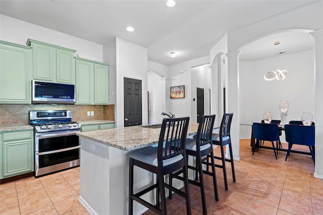 kitchen featuring ornate columns, a sink, green cabinetry, stainless steel appliances, and backsplash