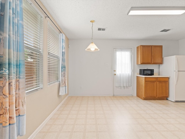 1728 Creek Bend Ln, Little Elm, TX 75068 - kitchen featuring a textured ceiling, black microwave, brown cabinets, freestanding refrigerator, and light floors