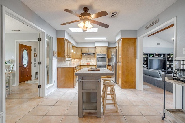 kitchen with appliances with stainless steel finishes, a center island, a ceiling fan, and visible vents