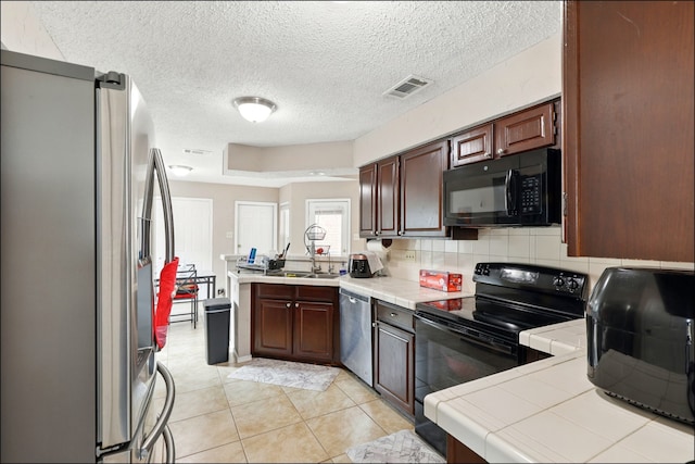 kitchen featuring black appliances, tile countertops, a peninsula, a sink, and a textured ceiling