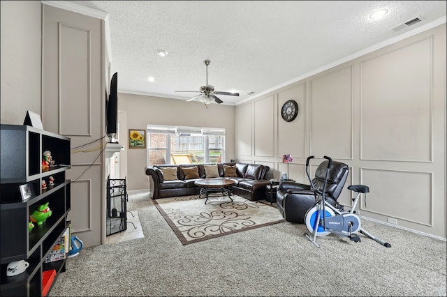 living room with a decorative wall, carpet flooring, a textured ceiling, ornamental molding, and a ceiling fan