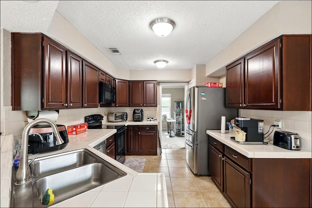 kitchen with black appliances, a sink, a textured ceiling, decorative backsplash, and light tile patterned floors