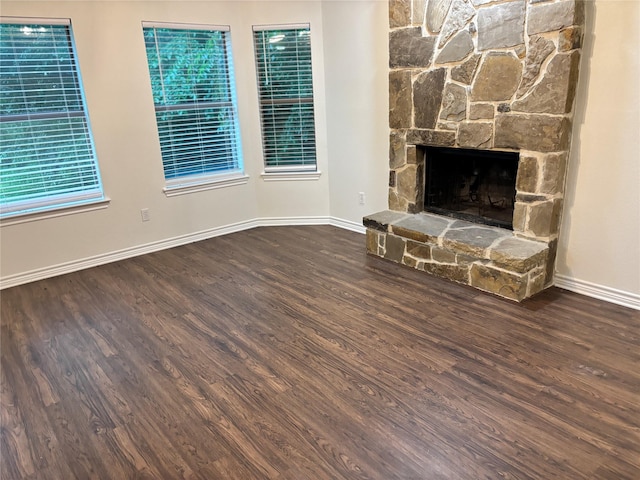 unfurnished living room with baseboards, a stone fireplace, and wood finished floors
