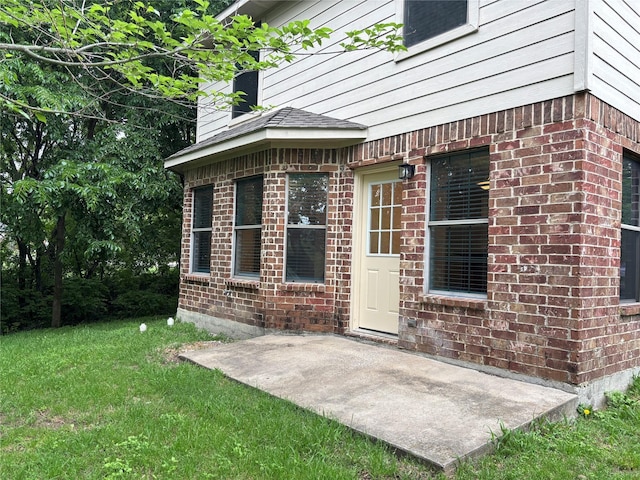 doorway to property featuring brick siding, a patio area, and a lawn