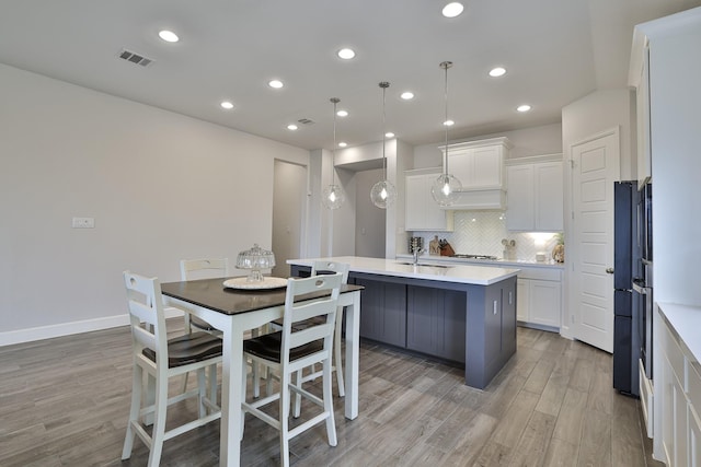 kitchen featuring white cabinetry, decorative backsplash, light wood-type flooring, visible vents, and a center island with sink