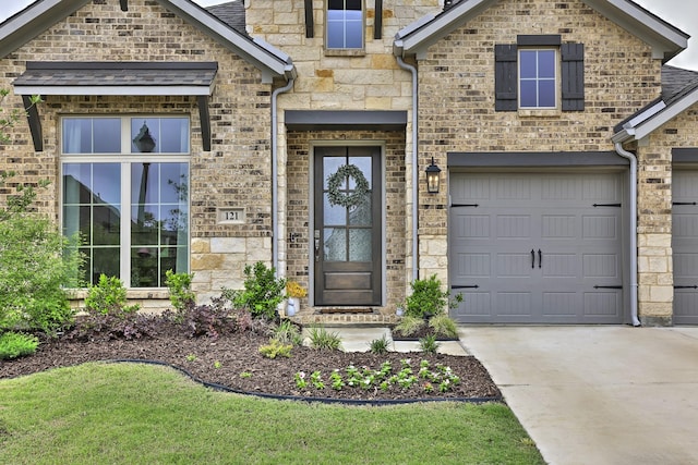 entrance to property featuring a garage, stone siding, and concrete driveway
