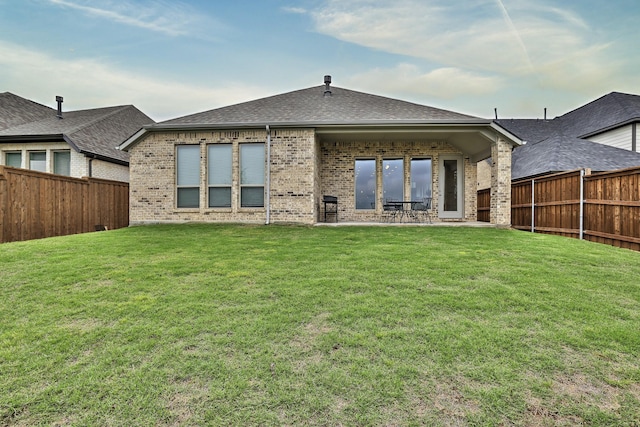 rear view of house featuring a yard, brick siding, and a fenced backyard