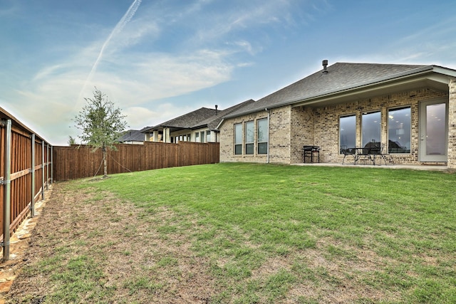 back of property featuring brick siding, a fenced backyard, a yard, and a shingled roof