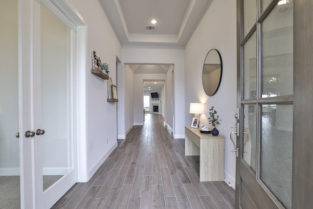 hall with baseboards, a tray ceiling, wood finished floors, and visible vents