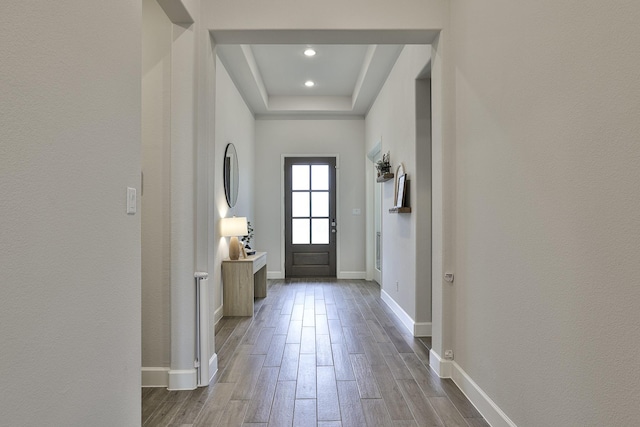 doorway to outside featuring recessed lighting, baseboards, wood finished floors, and a tray ceiling