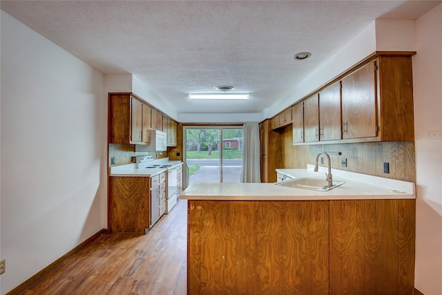 kitchen featuring a textured ceiling, light wood-type flooring, a sink, a peninsula, and white appliances