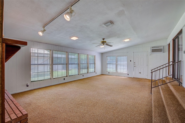 unfurnished living room with carpet floors, a wall mounted air conditioner, lofted ceiling, and a healthy amount of sunlight