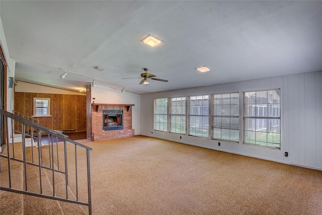 unfurnished living room featuring wooden walls, carpet floors, ceiling fan, and a brick fireplace