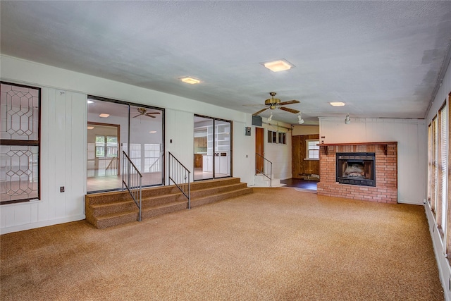 unfurnished living room featuring carpet floors, stairs, ceiling fan, and a brick fireplace