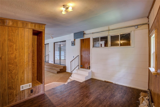 unfurnished room with a textured ceiling, visible vents, wood walls, wood finished floors, and stairs