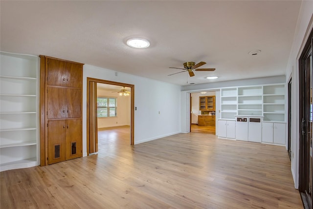 empty room featuring a ceiling fan, baseboards, built in features, and light wood-type flooring