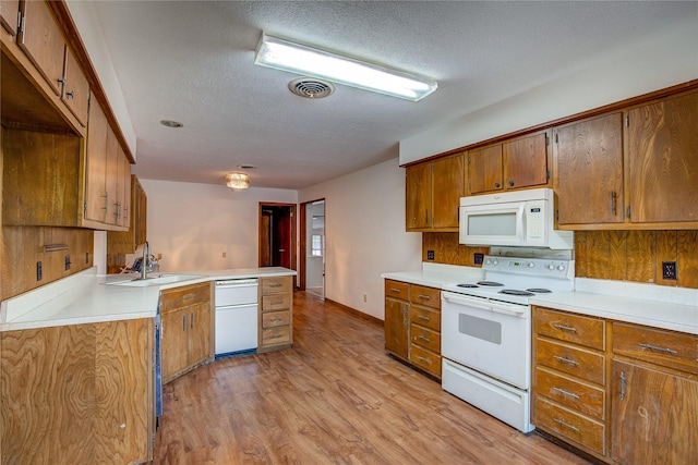 kitchen featuring a textured ceiling, brown cabinets, light wood-type flooring, a sink, and white appliances