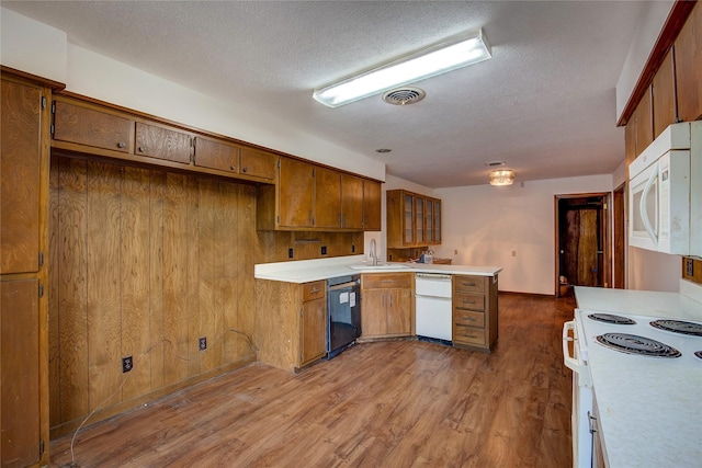 kitchen featuring a textured ceiling, a sink, light countertops, a peninsula, and white appliances