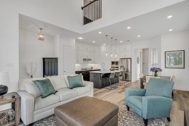 living area with recessed lighting, baseboards, light wood finished floors, and a towering ceiling